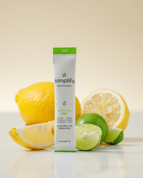 Simplify Electrolytes lemon lime 1000 stick with fresh lemon and lime on a warm cream backdrop
