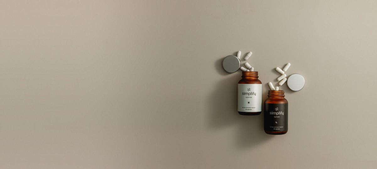 Simplify Sunrise and Sunset vitamin bottles, caps off with capsules spilled, flat lay on a warm greige backdrop